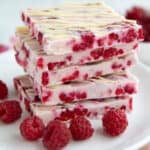 A stack of keto raspberry frozen yogurt bark squares on a white plate with fresh raspberries.