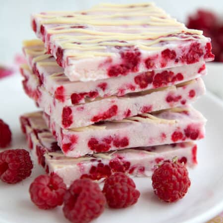 A stack of keto raspberry frozen yogurt bark squares on a white plate with fresh raspberries.