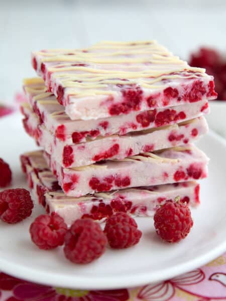 A stack of keto raspberry frozen yogurt bark squares on a white plate with fresh raspberries.