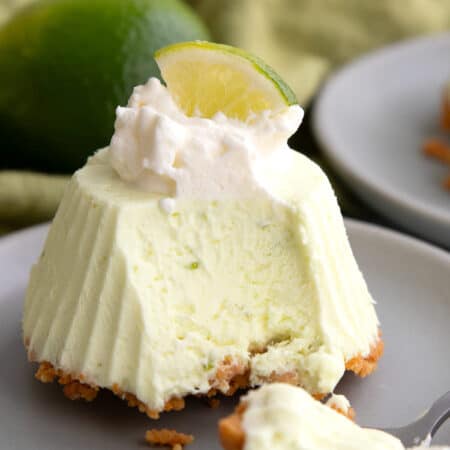 A Keto Frozen Key Lime Pie on a small gray plate with whipped cream and a lime slice on top, and a spoonful taken out of it.