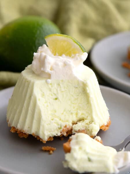 A Keto Frozen Key Lime Pie on a small gray plate with whipped cream and a lime slice on top, and a spoonful taken out of it.