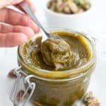 A spoon digging into keto pistachio cream in a glass jar.
