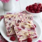Squares of keto frozen yogurt bark with raspberries on a white plate over a pink floral napkin.
