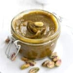 Close up shot of Keto Pistachio Cream in a small jar, with pistachios scattered around the bottom.