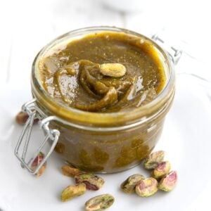 Close up shot of Keto Pistachio Cream in a small jar, with pistachios scattered around the bottom.