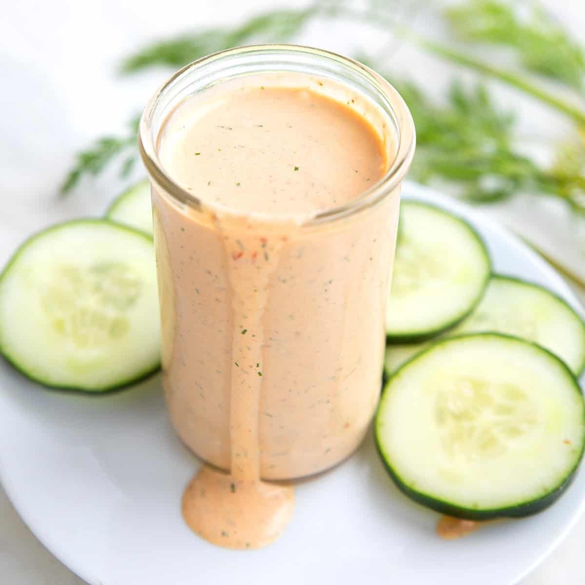 A glass jar filled with chipotle ranch dressing, surrounded by cucumber slices and sprigs of dill.