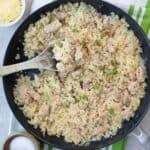 Top down image of a pan filled with creamy chicken and cauliflower rice over a white and green striped napkin.