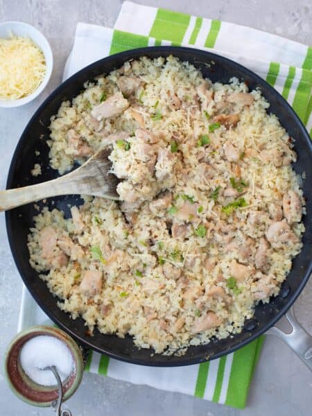 Top down image of a pan filled with creamy chicken and cauliflower rice over a white and green striped napkin.