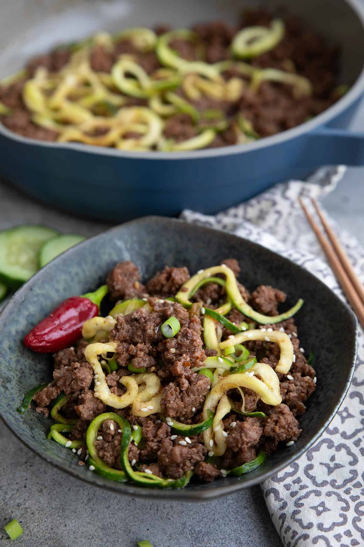 Keto Korean Beef with Zucchini Noodles in a black bowl, with the pan of more Korean beef in the background.