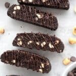 Titled image top down of keto chocolate hazelnut biscotti laid out on a white table, with chocolate drizzle over each one.