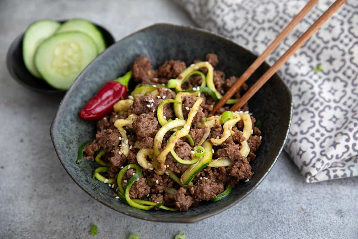 Close up shot of a black bowl filled with Keto Korean Beef and Zucchini Noodles, with chopsticks sticking out of it.