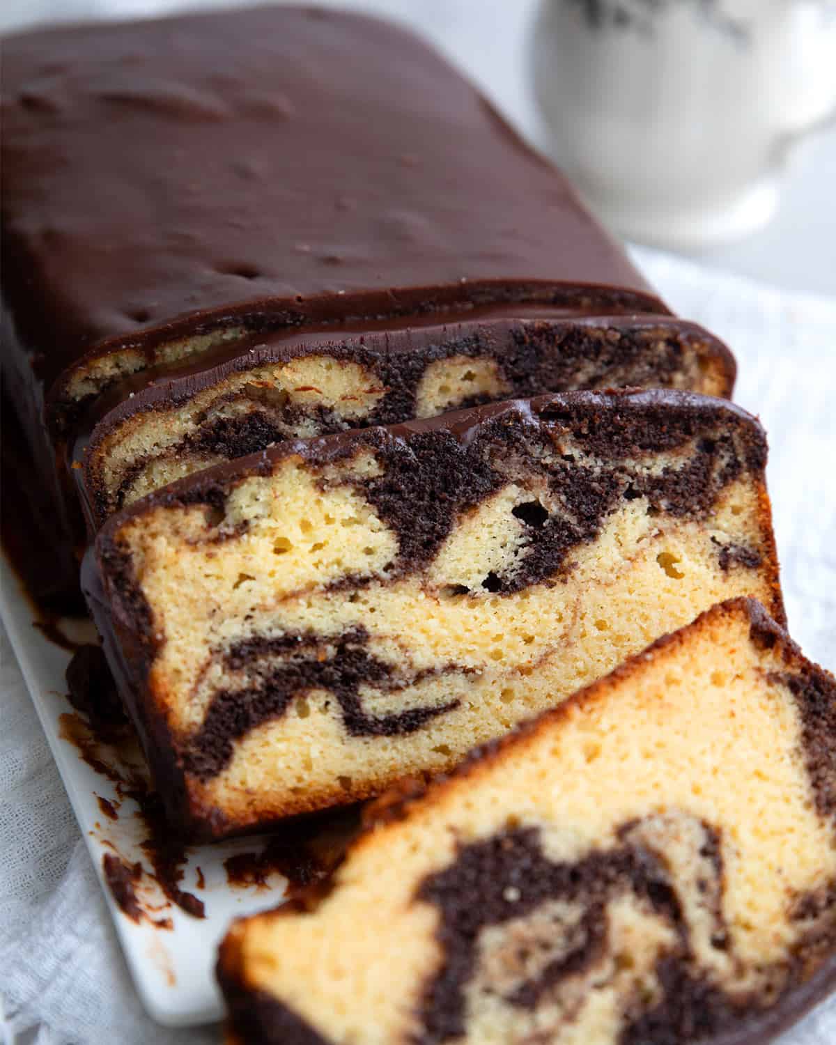 Keto Marble Pound Cake with chocolate glaze cut into slices on a white platter.