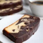 A slice of keto marble pound cake on a white plate with a cup of coffee in the background.