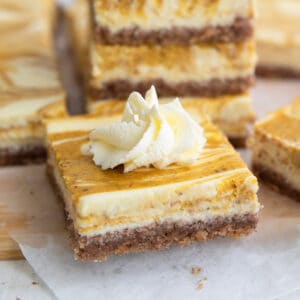 Close up shot of a keto pumpkin swirl cheesecake bar with a dollop of whipped cream on top.