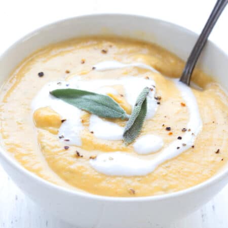 A white bowl filled with keto pumpkin soup with sage leaves on top and a spoon digging into it.