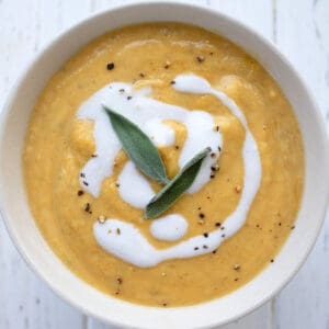 Top down image of a bowl of keto pumpkin soup with a swirl of cream and two sage leaves on top.