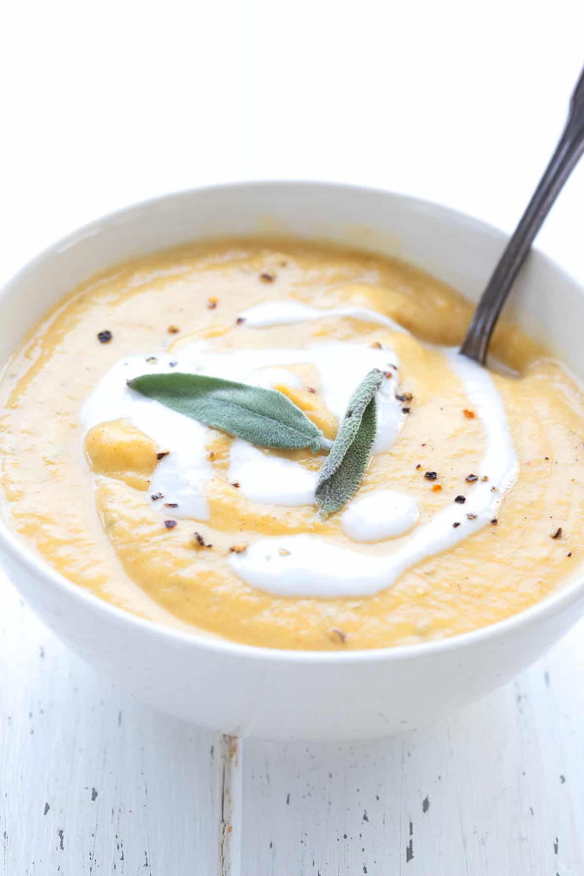 A white bowl filled with keto pumpkin soup with sage leaves on top and a spoon digging into it.