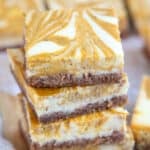 Close up shot of a stack of four keto pumpkin swirl cheesecake bars, with more bars in the background.