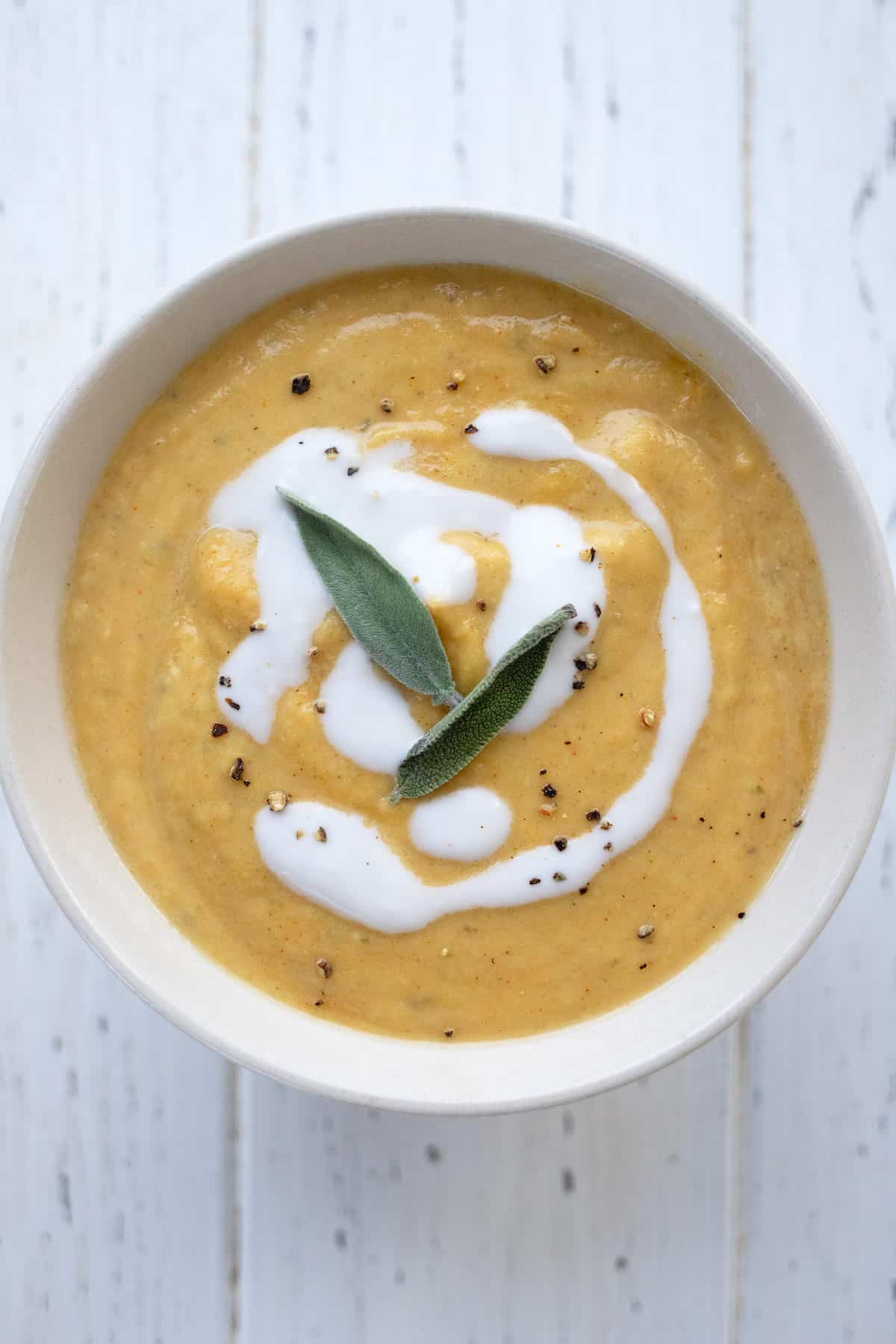 Top down image of a bowl of Keto Pumpkin Soup with a swirl of cream and two sage leaves on top.