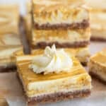 A keto pumpkin swirl cheesecake bar on a cutting board, with a stack of more cheesecake bars in the background.
