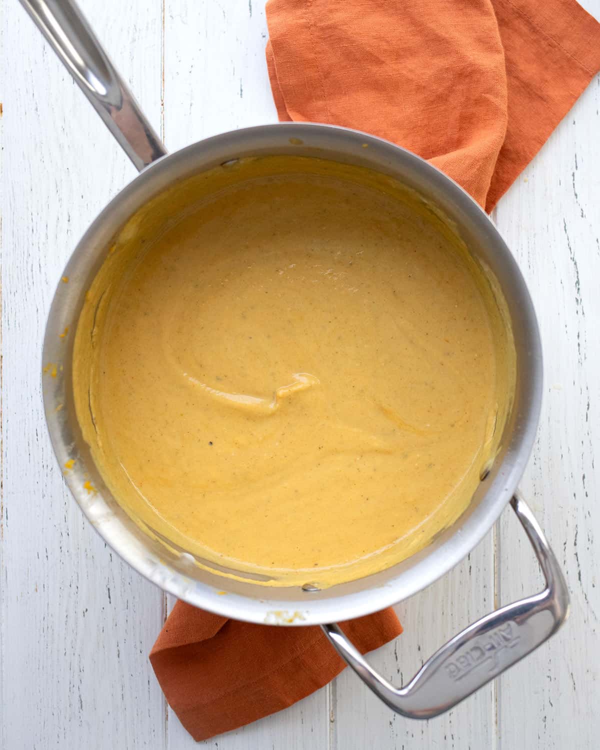 A large metal pot filled with creamy keto pumpkin soup, sitting on an orange napkin.