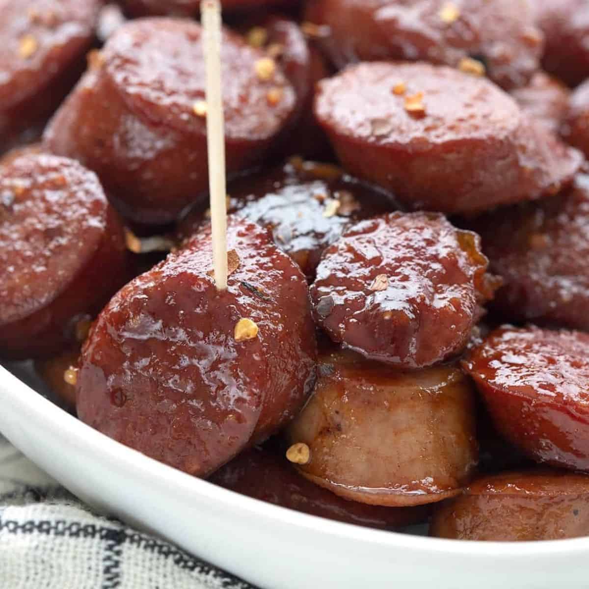Close up shot of keto kielbasa bites in a white bowl, with a toothpick sticking out of one.