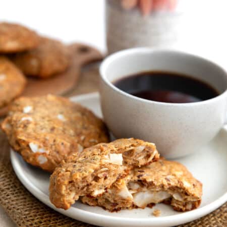 Two Keto Maple Breakfast Cookies on a white plate with a cup of coffee, with the front one broken in half.