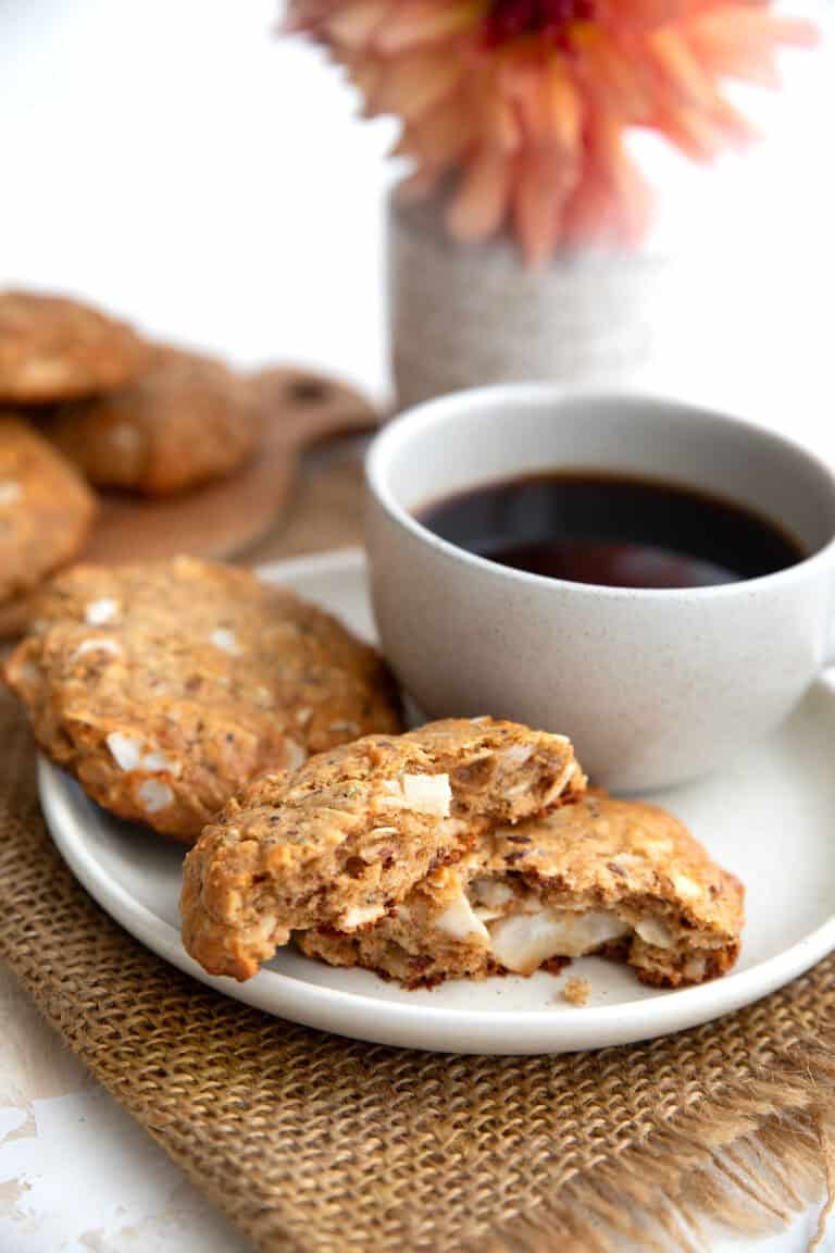 Two Keto Maple Breakfast Cookies on a white plate with a cup of coffee, with the front one broken in half.