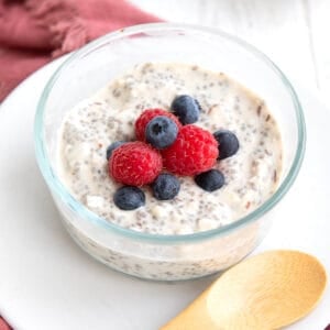 Close up shot of a small glass bowl filled with keto overnight oats topped with fresh raspberries and blueberries.