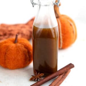 Close up shot of a glass bottle filled with keto pumpkin spice syrup, with two cinnamon sticks and a star anise in front.
