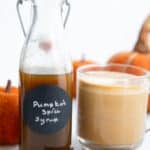 A bottle of Keto Pumpkin Spice Syrup beside a cup of coffee with frothed milk.