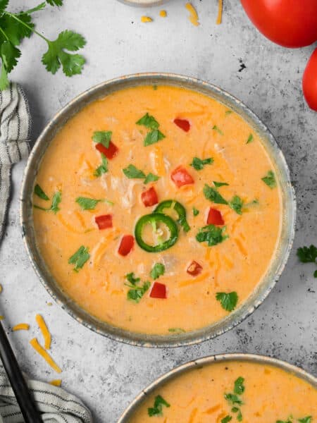 Top down image of Keto King Ranch Chicken Soup in a rustic gray bowl with chopped tomatoes, cilantro, and slice jalapeno on top.