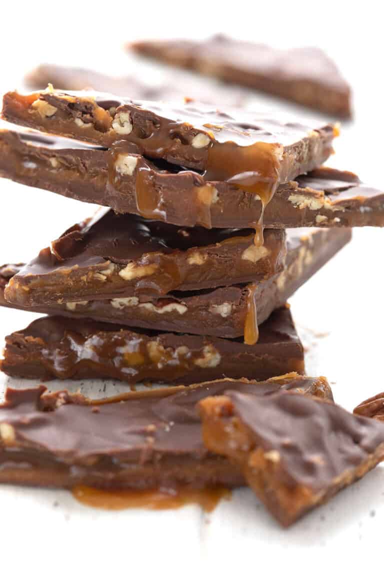Close up shot of a stack of keto pecan caramel bark on a white wooden table.