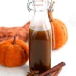 A bottle of Keto Pumpkin Spice Syrup on a white table with decorative pumpkins, cinnamon sticks and a star anise.